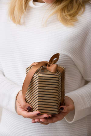 Closeup of nicely wrapped birthday, Christmas or any celebration gift in woman's hands. Girl holding present wrapped in brown paper and decorated with satin ribbon.の写真素材