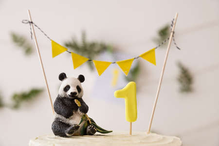 Closeup of beautiful white birthday cake. Celebration delicacy. Healthy carrot cake for 1 year old baby decorated with toy panda and flags banner and fern leaves. Holiday  idea.の写真素材