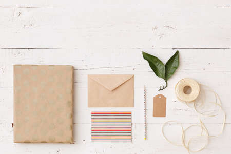 Top view on a gift wrapped in paper with dots for Christmas, birthday, or any other holiday. Postcard, envelope, ribbon, pencil and tag on a white wooden background. holiday and celebration conceptの写真素材
