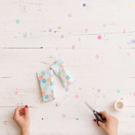 Top view on girl's hands wrapping nice Christmas or birthday gift on white wooden table background with confetti.の写真素材
