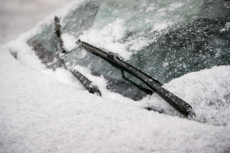 Car wiper blades clean snow from car windows. Flakes of snow covered the car with a thick layer. Safe driving with working wipers and clean windshield.の写真素材