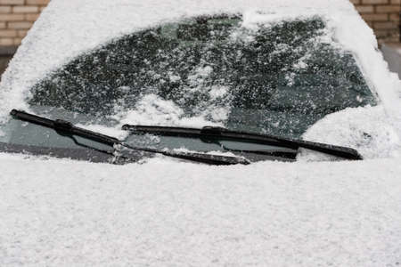 Car wiper blades clean snow from car windows. Flakes of snow covered the car with a thick layer....
