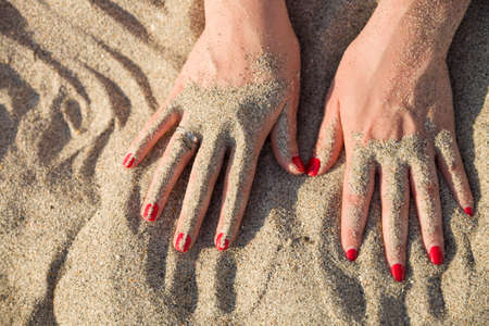 Beautiful girl hands sunk in the sand. Young woman with engagement ring. Honeymoon on the sea beachの写真素材