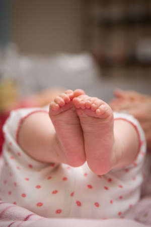 Closeup of a newborn baby feet in pants. Childhood. Little bare feet of a little girl. Newborn baby with mom. Indoorsの写真素材