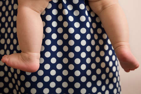 Closeup of baby's bare feet on the background of my mother's dress with polka dots. Woman holding a...