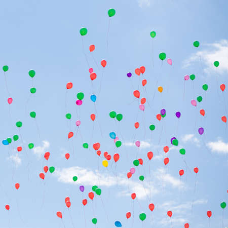 Many colorful balloons fly in the blue sky. Bright festive event. Blue sky and clouds