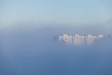 A lonely tall building peeking out from under a dense layer of fog that covered the city in the...