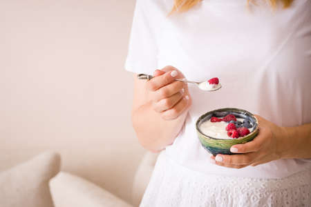 Young woman with a bowl of yogurt. Girl eating organic yogurt for breakfast with fresh berries in a bowl. Girl holding homemade healthy yogurt with raspberries and blueberries.の写真素材