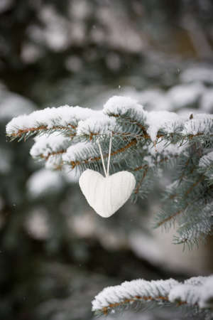 Closeup of beautiful knitted heart Christmas decoration on a evergreen tree with snow. Winter, Christmas celebration, holidays season conceptの写真素材
