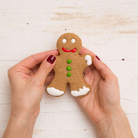 Girl holds cookies in the shape of a Gingerbread man in hands on a white wooden background. Top view...