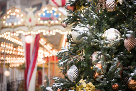 Big beautiful toys hang on a Christmas tree, hung with sparkling garlands and covered with snow. New Year decorations on the streets of Moscow. Christmas fir tree on the background of a carousel. Selective focusの写真素材