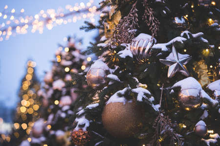 Evergreen tree with toys and sparkling garlands covered with snow against the background of the night sky and blurry garlands. New year decorations in the center of Moscow. Toning and artificial noiseの写真素材