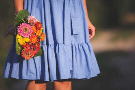 A young girl in a blue dress holds in her hand a beautiful bouquet of wildflowers on a sunny day. A bouquet of colorful flowers in a woman's hand. Toningの写真素材