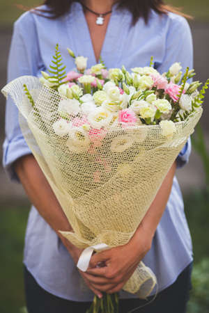 Closeup of a beautiful bunch of beautifully packaged garden roses in woman's hands. Girl in a blue shirt with summer flowers on a sunny summer day. Toningの写真素材