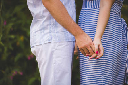 A man and a woman are holding hands while walking in a park on a sunny day. A love couple spends time together. Love, marriage and happiness.の写真素材
