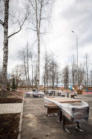 Empty playground with tables covered with polyethylene film and other equipment in the city park is fenced with warning tapes in red and white. Coronavirus pandemic covid-19 in the world. Stay at homeの写真素材