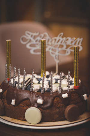 A close-up of chocolate birthday cake. Holiday treat. Healthy cake for a child, decorated with candles and fireworks with the word in Russian - Congratulations, in the background. Toningの写真素材