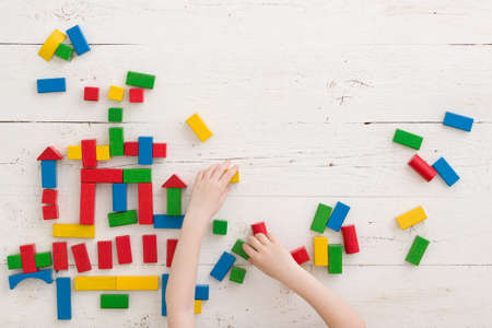 Top view on wooden colorful bricks on a white wooden background. A child builds a castle out of...
