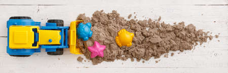 Kinetic sand with colorful molds removes a tractor with a bucket from the table. Top view on colorful sand molds and other toys on a white wooden table. Early development and education. Wide viewの写真素材