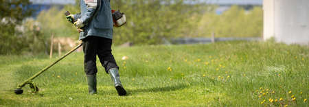A view from the back of a man with a lawn mower. Worker in protective clothing mows grass on the...