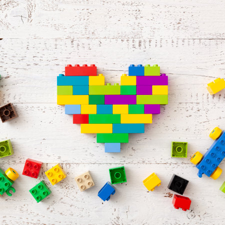 Multi-colored plastic cubes are scattered on a white wooden table. Creative building in the shape of a heart from a bright constructor. Early learning. Educational toysの写真素材