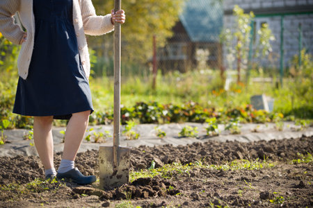 A girl with a shovel is resting next to the garden bed. Planting seeds of a new harvest. The girl helps her parents in the garden. Rural life concept.の写真素材