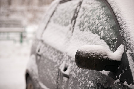 Early winter. Unexpected snow covered cars and roads. Door mirror and glass of a car in the snow. Road safety.の写真素材