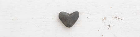 Small stone heart on a white background. Heart made of natural stone on a painted wooden board....