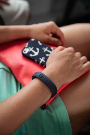 Close-up of female hands holding a smartphone and a pink handbag. A girl with a bag and a phone in...