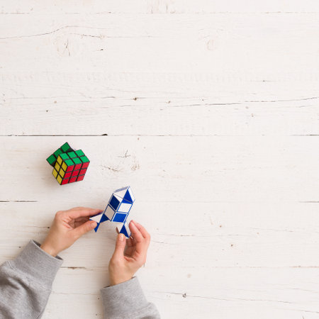 Moscow, Russia, February 16 2018: Rubik's snake puzzle in rocket shape in woman's hands, closeup, and Rubik's cube laying owhite wooden background. Girl holding Rubik's puzzle toy and playing with it.のeditorial素材