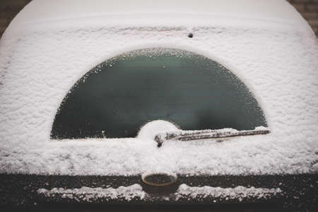 Snow suddenly fell on cars and roads. A car wiper cleans the rear glass from a thick layer of snow. Road safety. Selective focusの写真素材