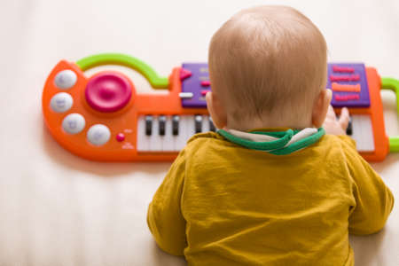 Top view on small cute baby boy sitting on the sofa and playing on the toy piano. A little boy...