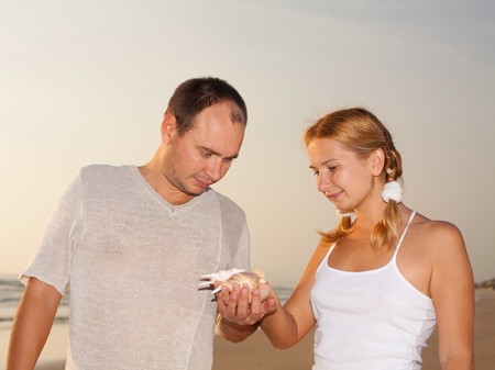 Young couple looking on seashell near oceanの写真素材