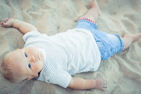 Cute baby lying down on a sandの写真素材