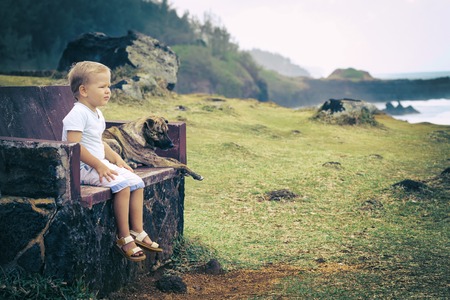 Child and dog are sitting on a bench and looking seaの写真素材