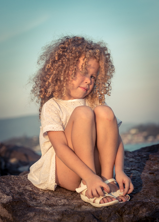 Little girl in white dress on a rock near a seaの写真素材