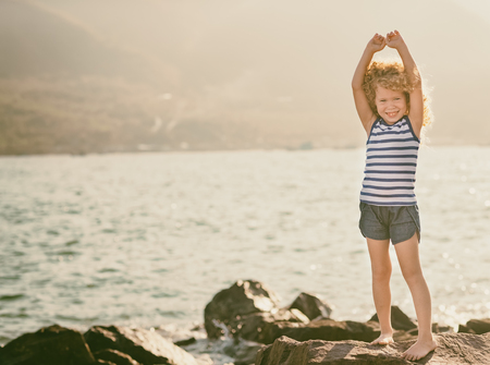 Little girl with with raised hands on a rock near a seaの写真素材