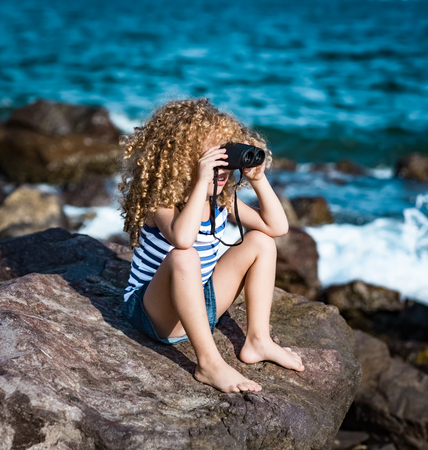 Little girl looking far away with binoculars, sitting on a rock near a seaの写真素材