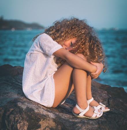 Little girl in white dress on a rock near a seaの写真素材