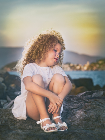 Little girl in white dress on a rock near a seaの写真素材