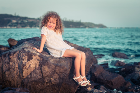 Little girl in white dress on a rock near a seaの写真素材