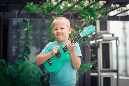 Portrait of a cute boy sitting ouddoor with ukuleleの写真素材