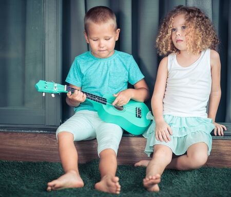 Portrait of a cute kids sitting ouddoor with ukuleleの写真素材
