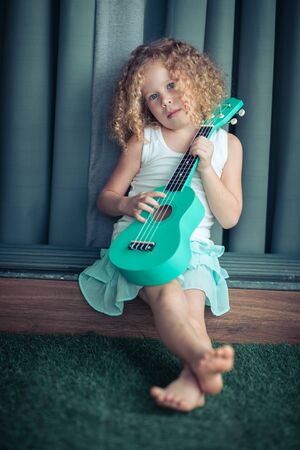 Portrait of a cute girl sitting ouddoor with ukuleleの写真素材