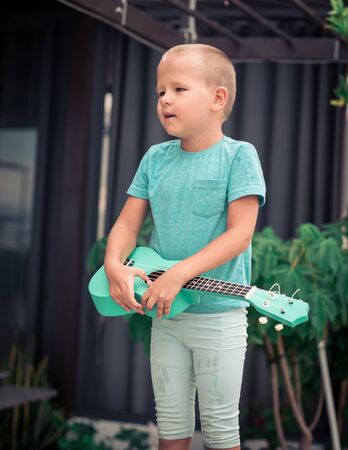 Portrait of a cute boy sitting ouddoor with ukuleleの写真素材