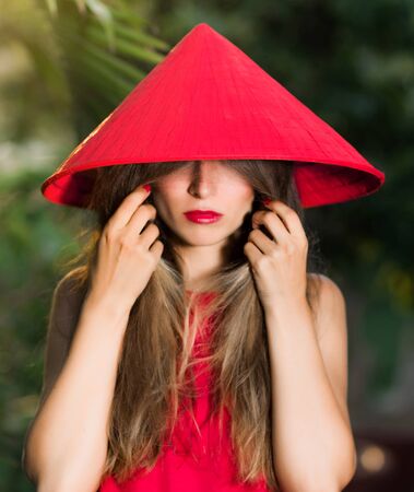 Fashion portrait of a beautiful woman in red conical hat outdoorの写真素材