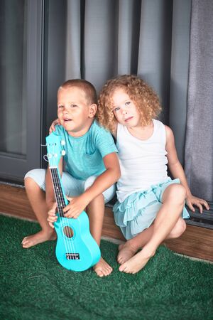 Portrait of a cute kids sitting ouddoor with ukuleleの写真素材