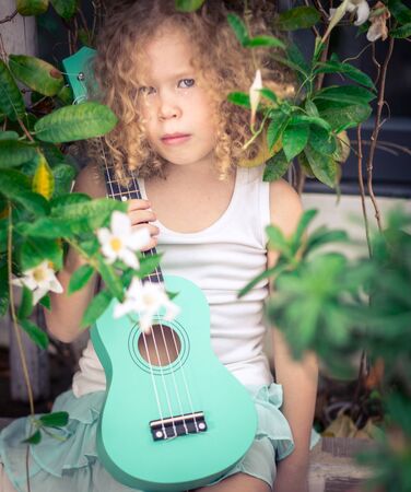 Portrait of a cute girl sitting ouddoor with ukuleleの写真素材