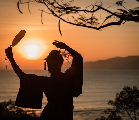 Silhouette of Japanese Geisha in kimono with fan at sunriseの写真素材