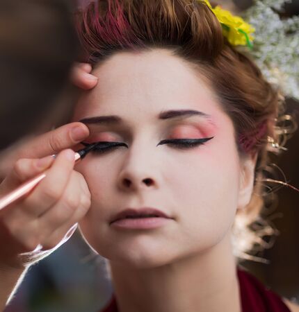 Portrait of a beautiful woman in beauty salon. Makeup artist applies eyeliner on a faceの写真素材